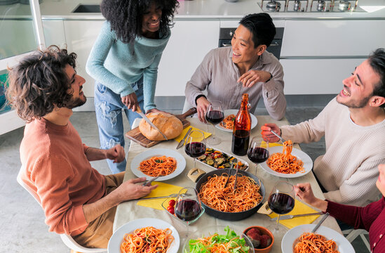 black girl cutting bread - Smiling friends are having a lunch party at home - People laughing while eating spaghetti - Friendship life style concept with young people having fun together at home