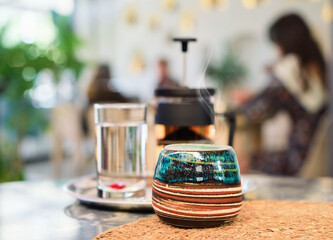 beautiful handmade cup for tea on a table in a cafe, steam from tea rises above the teacup, selective focus, blurred background. meeting with friends in a cafe, sustainable social development.