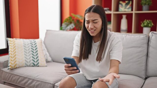 Young beautiful hispanic woman using smartphone with angry expression at home