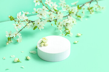 Decorative podium and blooming branch on green background