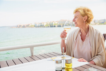 Mature attractive woman traveler sitting alone on the terrace of coffee shop and drinking rose...