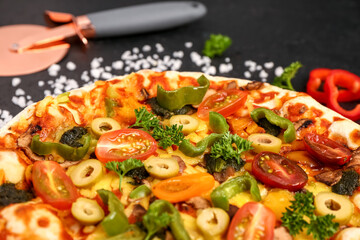 Vegetable pizza with cutter on dark background
