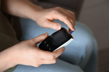 Woman with diabetes measuring blood sugar level at home, closeup