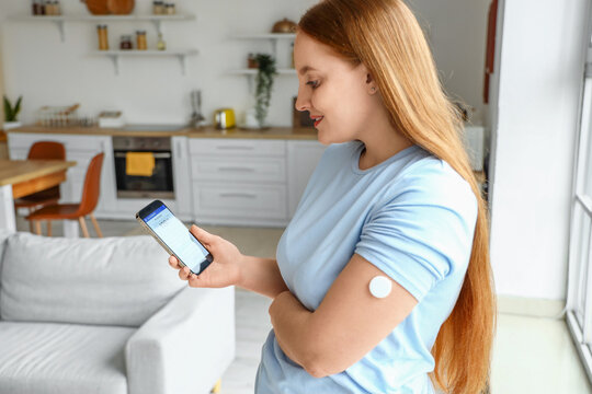 Woman with glucose sensor using mobile phone for measuring of blood sugar level at home