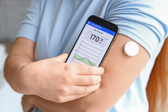 Woman with glucose sensor using mobile phone for measuring of blood sugar level, closeup