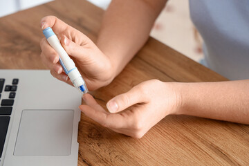 Woman with diabetes taking blood sample at home, closeup