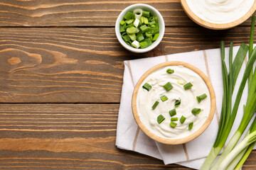 Bowls of tasty sour cream with green onion on wooden background