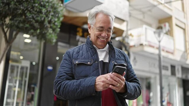 Middle age man with grey hair using smartphone smiling at street