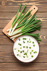 Bowl of tasty sour cream with green onion on wooden background