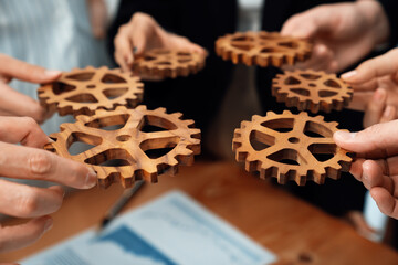 Closeup hand holding wooden gear by businesspeople wearing suit for harmony synergy in office...