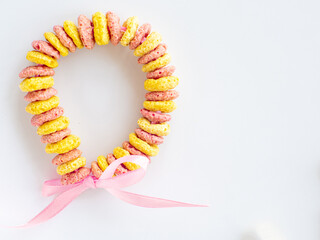 Edible DIY bracelet or necklace for Mothers day. DIY for kids. Bracelet made with froot ring shaped cereal. Making gift with fruit loops for Mothers day. Colored cereals background with copy space.