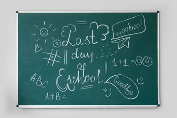 Blackboard with text LAST DAY OF SCHOOL and drawings on light wall in classroom