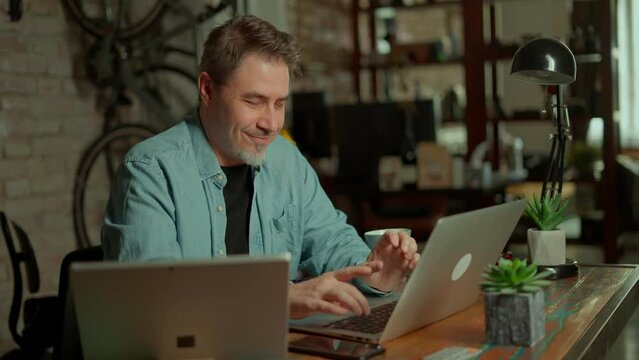 Entrepreneur working sitting at a desk typing on laptop computer in home office. Portrait of happy smiling caucasian man at home.