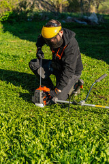 Man starting the engine of a lawn trimmer while wearing protective gear in green country side garden