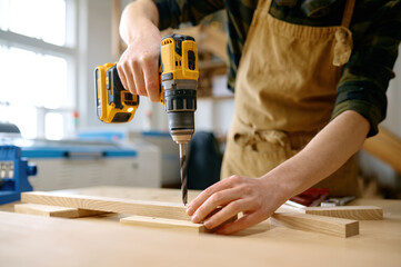 Carpenter working with drill leaning over table at carpentry workshop - obrazy, fototapety, plakaty