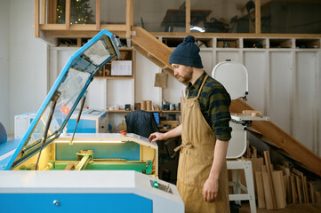 Naklejka na ściany i meble Man carpenter operating CNC laser machine in automated woodworking studio