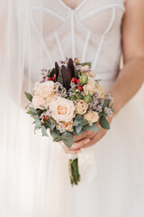 Beautiful wedding bouquet with protea and roses in the hands of the bride