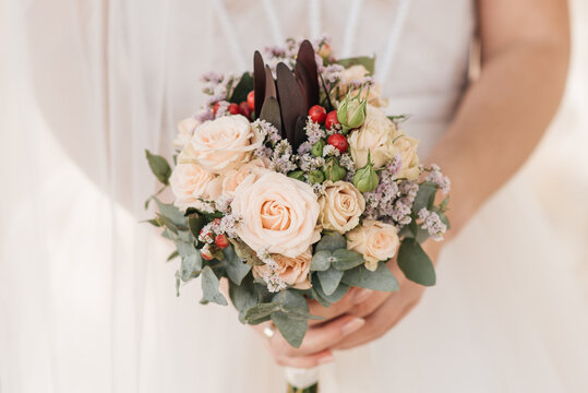 Beautiful wedding bouquet with protea and roses in the hands of the bride