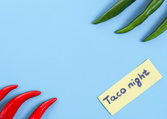 Spicy green and red chili peppers lie on the sides with a yellow taco night note on a light blue