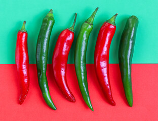 Six hot green and red chili peppers lie horizontally in a row on a red-green background
