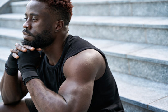 Fit confident sporty young black man boxer fighter sitting outdoors. Strong African ethnic guy relaxing after street workout exercises or boxing, resting after training outside. Portrait