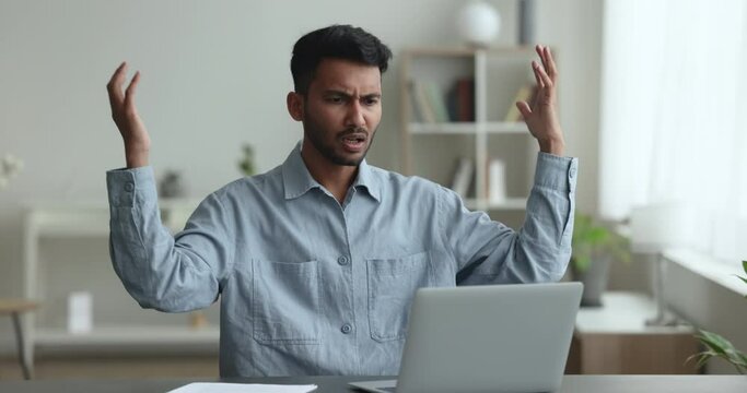 Annoyed angry 35s Indian businessman troubled with sudden computer failure, sit at desk looks at laptop screen gesturing feels mad due to hanging broken device, virus attack, incorrect Generative AI