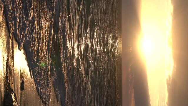 Ocean waves with foam on sandy beach and beautiful golden sunset in sky.