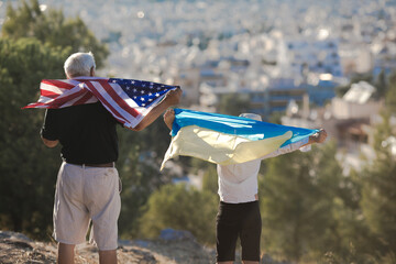 Retired man  and kid boy holding the flags of the USA and Ukraine on city  view