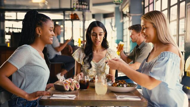 Group of multi-cultural female friends meeting in restaurant taking photo of food on mobile phone and posting to social media - shot in slow motion