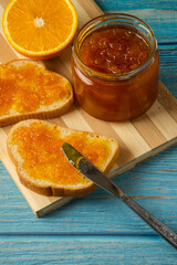 Delicious toasts with sweet jams on marble background, Raspberry jam set. Confiture spread on piece of toast bread, knife, glass jar with jelly, spoon, bowl and fresh red strawberry