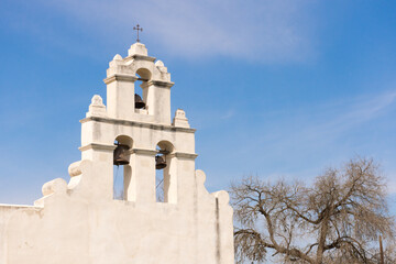 The pure white adobe of Mission San Juan bell tower and cross bathed in sunlight