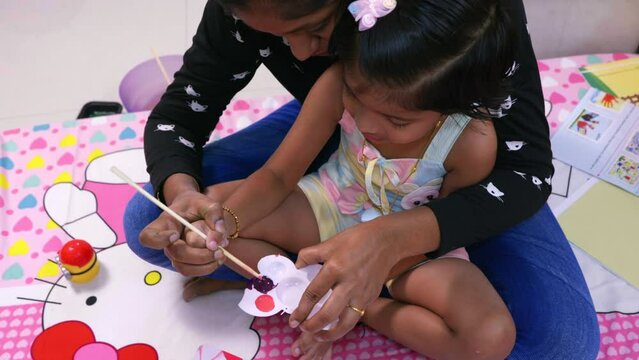 indian mom and daughter mixing color before they start to pain on color paper brown white and pink