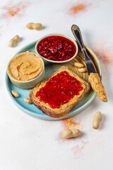 Delicious toasts with sweet jams on marble background, Raspberry jam set. Confiture spread on piece of toast bread, knife, glass jar with jelly, spoon, bowl and fresh red strawberry