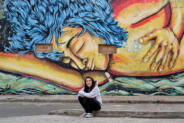 Joven sentada en la acera disfrutando con mural de fondo © Patricia Molaioli