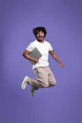 Happy man with laptop jumping on purple background