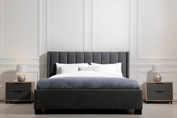 Comfortable bed between bedside tables with lamps at home. Interior design