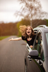 a happy girl with her hair fluttering in the wind looks out of the car window on a summer day.