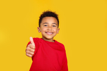 African-American boy showing thumb up on yellow background. Space for text © New Africa