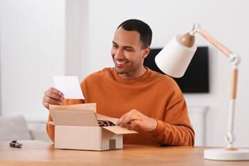 Happy young man with greeting card near parcel at wooden table. Internet shopping