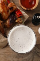 Glass of beer, delicious baked chicken wings and sauce on wooden table, closeup