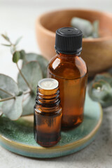 Bottles of eucalyptus essential oil and plant branches on light grey table