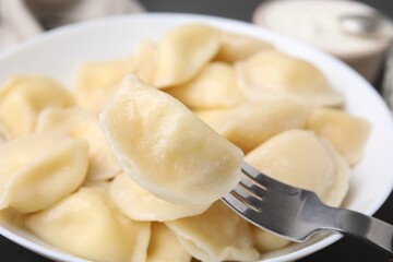 Fototapeta na wymiar Delicious dumpling (varenyk) with cottage cheese on fork over bowl, closeup