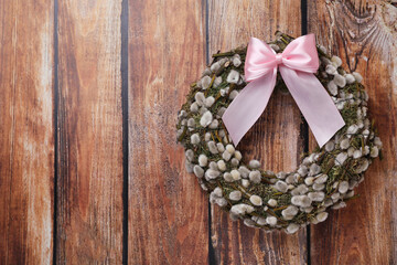 Wreath made of beautiful willow branches and pink bow on wooden background, top view. Space for text