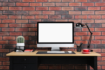Stylish workplace with computer, lamp and stationery on wooden table near brick wall