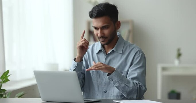 Indian deaf guy communicates with sign language sit at desk with laptop, having personal or business conversation showing fingers gestures, take part in on-line meeting using video call Generative AI