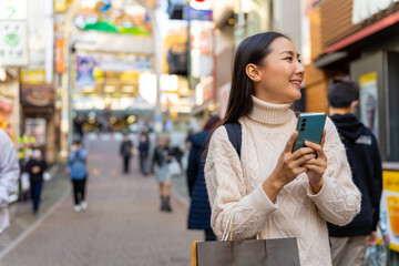 Happy Asian woman walking with using mobile phone during shopping at Tokyo city, Japan. Attractive girl enjoy outdoor lifestyle travel city street with using wireless technology on holiday vacation.