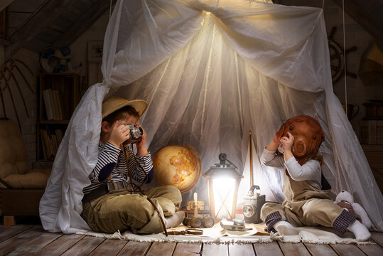 Children play in the attic of their house. Imagine themselves as tourists, explorers. Look through a telescope, study a world map, play in a makeshift tourist tent. Dreaming of travel and adventure.