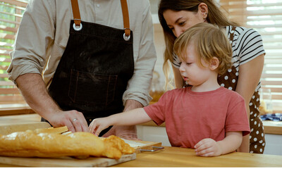 Obraz na płótnie Canvas Happy young family enjoying making pie dough or pastries in modern kitchen together, very happy parents teaching little son how to cook bakery at home.