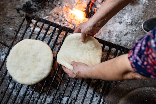 Manos apoyando tortilla casera asada en parilla con le&ntilde;a