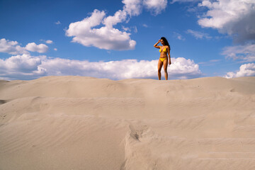 Young woman in yellow bikini walking on sand dune , sky background . Wide shot